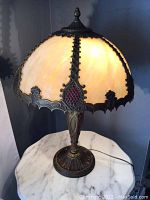 Side view of lamp illuminated showing dome-shaped stained glass shade with intricate metal framing and red glass accents.
