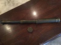 Vintage brass periscope fully extended placed on wood surface with brass cap beside it.