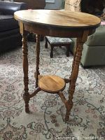 Full view of the round wood side table showing the turned legs, lower shelf, and tabletop surface.