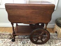 Front view of the wooden tea trolley closed with visible decorative carving and large and small wheels on opposite sides.