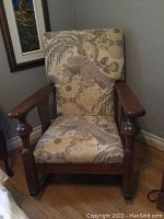 Front view of wooden rocking chair showing upholstered cushioned back and seat with floral and bird pattern.