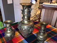 Set of three yellow brass urns on a colorful cloth, showing the overall appearance and relative sizes