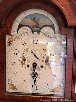 Close-up of the painted enamel clock face showing two birds, fruit motifs, Arabic numerals, subsidiary seconds dial, two semicircular date dials and painted sailing ship scene on the arch of the dial.