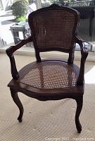 Full view of the antique dark oak and wicker chair positioned indoors with natural light, showing condition and details of wood carvings and wicker weaving.