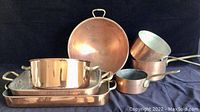 Front view of all five copper cookware pieces arranged on dark background