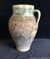 Photo of a brown and green ceramic jug with a single handle and glazed top section.