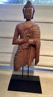 Wooden carved Buddha statue on solid black metal base.