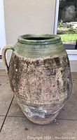 Tall ceramic jug with a single handle, green glaze near the top and earthy brown glaze below showing textured and weathered surface.