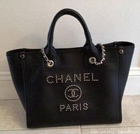 Front view of black leather bag with metal studded CHANEL logo and handles.