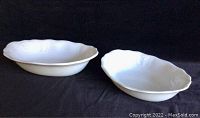 Photo of two white china serving bowls on black background, showing shape, size, and design detail