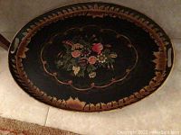 Top-down view of an oval wood painted decorative tray with black background, floral bouquet centerpiece, and gold leaf border.