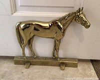 Front side view of a polished brass horse-shaped doorstop showing detailed horse figure and base.