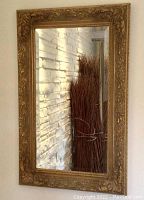 Full view of the gold framed baroque French mirror hanging on a wall with white stone background, showing the dimensions and details of frame and mirror glass.