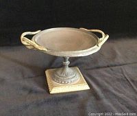 Photo of a decorative shallow bowl with Greek-style snake-shaped handles and pedestal base with ornamental details