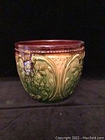 Front view of the green and yellow glazed ceramic flower pot with detailed floral embossed pattern and brown interior rim.