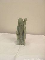 Green jade figurine of an old man holding a staff on a white cloth background.