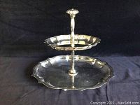 Two-tier sterling silver hors d’oeuvre platter with scalloped edges and decorative handle, displayed on black background.