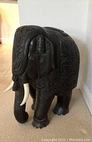 Front angled view showing black painted wood elephant with carved details and white tusks
