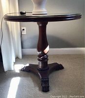 Side view of the mahogany coffee table showing the round glass top, central pedestal, and claw feet.