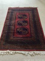 Photo showing rectangular red wool Belgian rug with three central medallions, intricate borders, and fringes at ends.