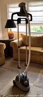 Full view of the Pur Steam garment steamer unit with extendable handle and hose, positioned next to furniture indoors.