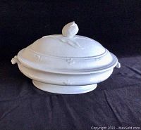 Oval white serving bowl with lid and tulip-shaped knob on black background