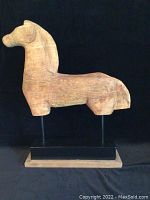 Front view of wooden horse sculpture mounted on black base and wooden platform, showing natural wood grain and stylized horse shape.