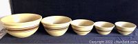 Front view of four ceramic bowls in a row by size on a black surface with a dark background.