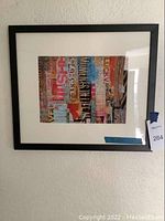 Framed collage art print showing colorfully layered text and images in a black frame on a light wall.