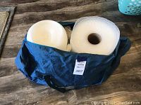 Blue bag with a roll of bubble wrap and white foam sheets inside, placed on wooden surface.