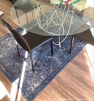 Blue area rug underneath a glass dining table with black chairs, showing its color and pattern.