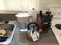 Photo showing a kitchen counter area with a Brita water filter pitcher, wooden knife block with multiple knives, stainless steel kettle, and paper towel holder.