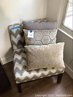 Chair upholstered in gray and cream geometric zigzag pattern with three decorative pillows placed on seat.