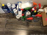 Photo showing a variety of cleaning products including sprays, disinfectants, polishes, and cleaning cloths with a metal rack in front.
