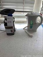 Photo showing Cuisinart coffee grinder with clear hopper and Toastmaster electric kettle on countertop