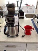 Photo of black and stainless steel Breville coffee maker with digital display, stainless steel thermal carafe, and black handle on kitchen counter with plug visible