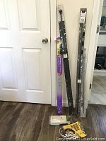 Curtain rods in original packaging leaning against white door on wood flooring, with plastic packaging and some accessories near base