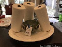 Photo showing a large white serving plate with six green ceramic bowls stacked inside and three rolls of paper towels on top.