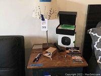 Overall lot display showing table lamp, thermostat box, batteries, and hooks on wooden side table