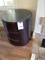 Full view of the round dark brown wooden end table on floor near window and fireplace.