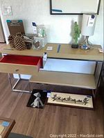 Front view of the modern sideboard showing light wooden surfaces, metal frame, single drawer opened revealing red interior, and some decorative items nearby (not included).