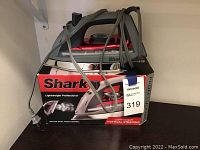 Shark Lightweight Professional Steam Iron in silver and black with red accents displayed on top of its original box with power cord loosely wrapped around the iron.