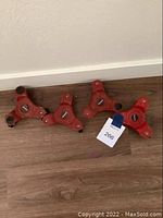 Four small red moving dollies with triangular shape and three black caster wheels each, resting on wood floor against a wall.