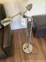 Photo showing metal standing lamp with two adjustable arms and light heads beside couch and ottoman.