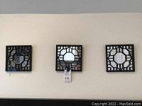 Three square wall hangings shown hung on a wall. Each has a central mirror and black geometric lattice frame.