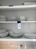 Wide view of white dishes on shelving showing multiple stacks of bowls, small plates, and larger plates mostly plain white.