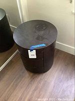 Front view of the round, dark wooden nightstand with three curved drawers, positioned against a wall and near a mirror.