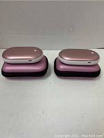 Two pink oval rechargeable portable hand warmers on top of their zipped carrying cases, front view showing overall size and color.