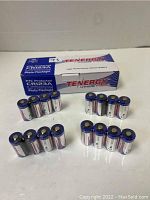 Box of Tenergy CR123A lithium batteries and groups of batteries arranged on a surface.