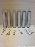 Front view of six under cabinet motion sensor LED lights lined up with six USB charging cables laid out in front.
